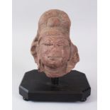 A 12TH CENTURY ISLAMIC CARVED RED SOAPSTONE HEAD on a wooden base, 17cm high.