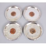 A SET OF FOUR ISLAMIC SILVER CIRCULAR DISHES inserted with coins, 11cm diameter.