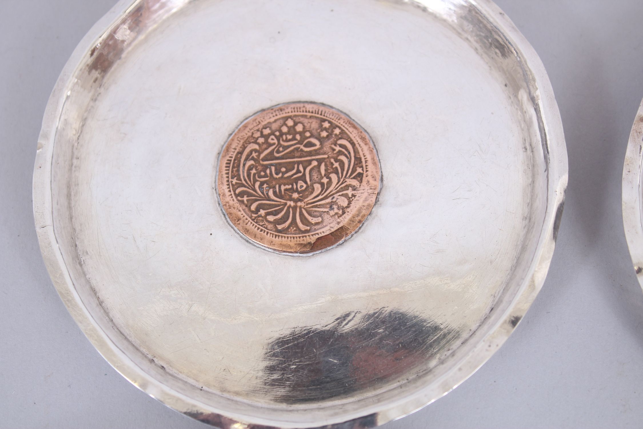 A SET OF FOUR ISLAMIC SILVER CIRCULAR DISHES inserted with coins, 11cm diameter. - Image 2 of 6