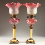A GOOD PAIR OF VICTORIAN CRANBERRY LAMPS AND SHADES, with onyx type stems and gilt metal. 57cms