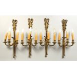 A SET OF FOUR CAST BRASS THREE BRANCH WALL APPLIQUES, with ribbon and bow decoration. 61cms high.