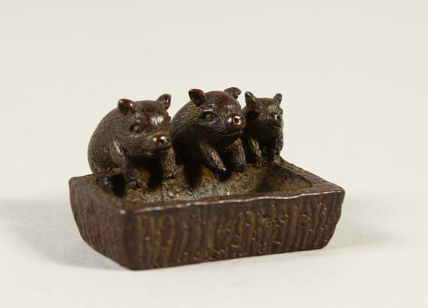 A SMALL BRONZE GROUP OF PIGS AT A TROUGH. 4.5cms wide.