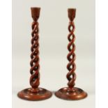 A PAIR OF BARLEY TWIST WOODEN CANDLESTICKS, on circular bases. 41cms high.