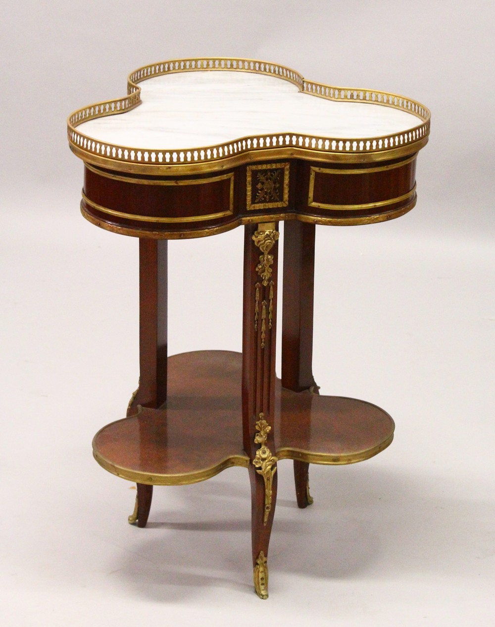 A FRENCH STYLE MAHOGANY, ORMOLU AND MARBLE TWO TIER TREFOIL SHAPE TABLE. 55cm wide x 75cm high.