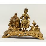AN ORNATE BRASS INKWELL, modelled as a young girl standing beside a thatched chicken coop. 24cms