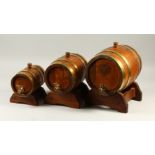 A GRADUATED SET OF THREE BRASS BOUND BARRELS ON STANDS. Largest 28cms long.