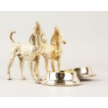 A PAIR OF CAST PLATE DOGS with a bowl. 12cms long.