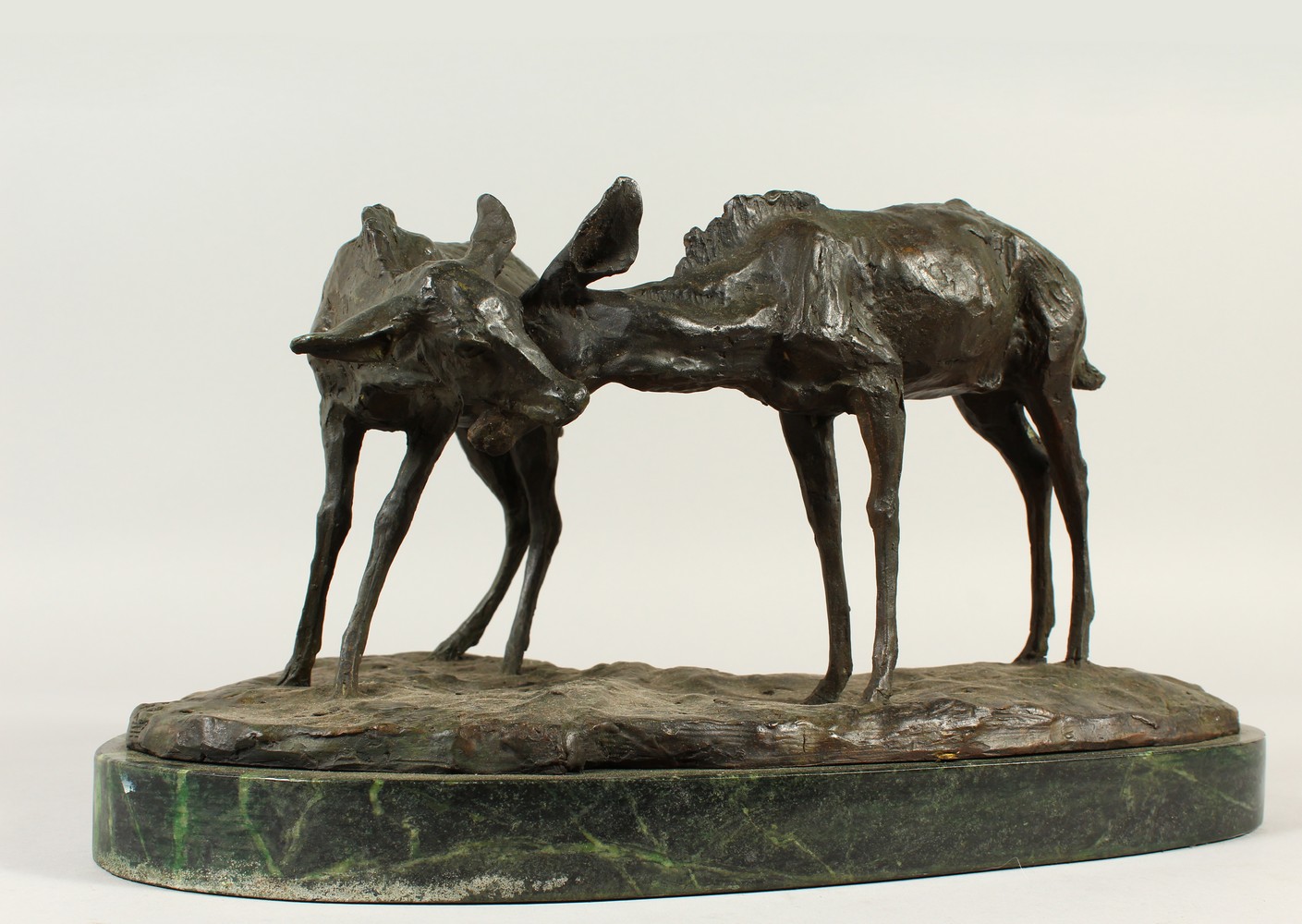 A NATURALISTIC CAST BRONZE GROUP OF TWO DEER, on a shaped marble base. 42cms wide.