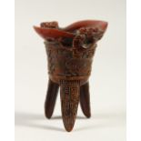 A CARVED HORN LIBATION CUP, on three legs. 11cms high.