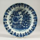 AN 18TH CENTURY TIN GLAZE BLUE AND WHITE PLATE, decorated with flowers and a fence. 29cms diameter.