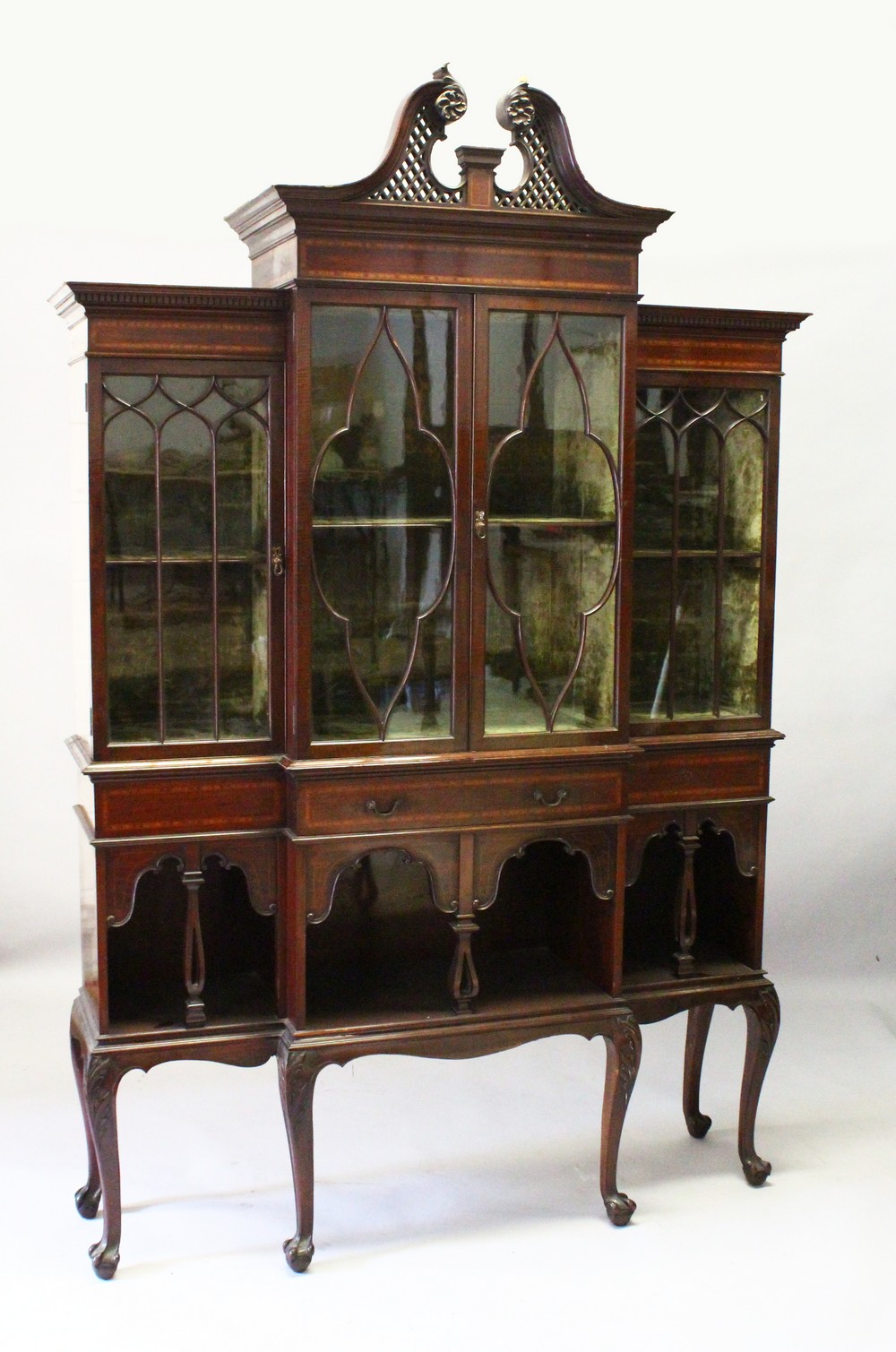 AN EDWARDIAN MAHOGANY BREAKFRONT STANDING BOOKCASE, the top with swan neck pediment, over four glass