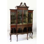 AN EDWARDIAN MAHOGANY BREAKFRONT STANDING BOOKCASE, the top with swan neck pediment, over four glass