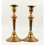 A PAIR OF 18TH CENTURY SEAMED BELL METAL CANDLESTICKS, on circular bases. 27cms high.
