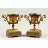A SMALL PAIR OF FRENCH METAL TWO-HANDLED URNS ON STANDS. 18cms high.