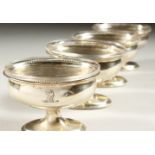 A SET OF FOUR GEORGE III OVAL PEDESTAL SALTS, with beaded edges and glass liners.