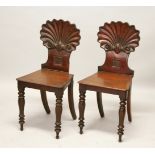 A GOOD PAIR OF REGENCY HALL CHAIRS, with carved shell backs, with solid seats, on turned legs.