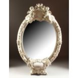 A LARGE MEISSEN WHITE PORCELAIN OVAL MIRROR, encrusted with flowers, with cupids holding a