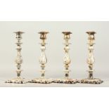 A SET OF FOUR PLATED CANDLESTICKS, on square bases. 30cms high.