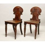 A PAIR OF LATE REGENCY MAHOGANY HALL CHAIRS, with carved shaped backs, solid seats, on turned legs.