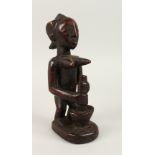 A GOOD CARVED WOOD TRIBAL FIGURE, female grinding corn. 21cms high.