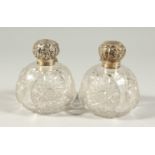 A PAIR OF VICTORIAN CUT GLASS GLOBULAR SCENT BOTTLES with silver repousse tops. 4INS DIAMETER.