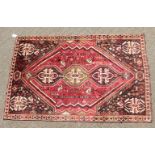 A PERSIAN TRIBAL SHIRAZ QASHQAI CARPET with a large motif on a red ground. 11ft 6ins x 5ft 6ins.