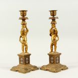 A PAIR OF 19TH CENTURY FRENCH CUPID CANDLESTICKS on enamel coloured columns. 10.5ins high.