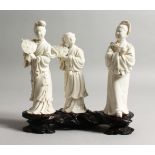 A SET OF THREE CHINESE BLANC DE CHINE FIGURES on a wooden stand.