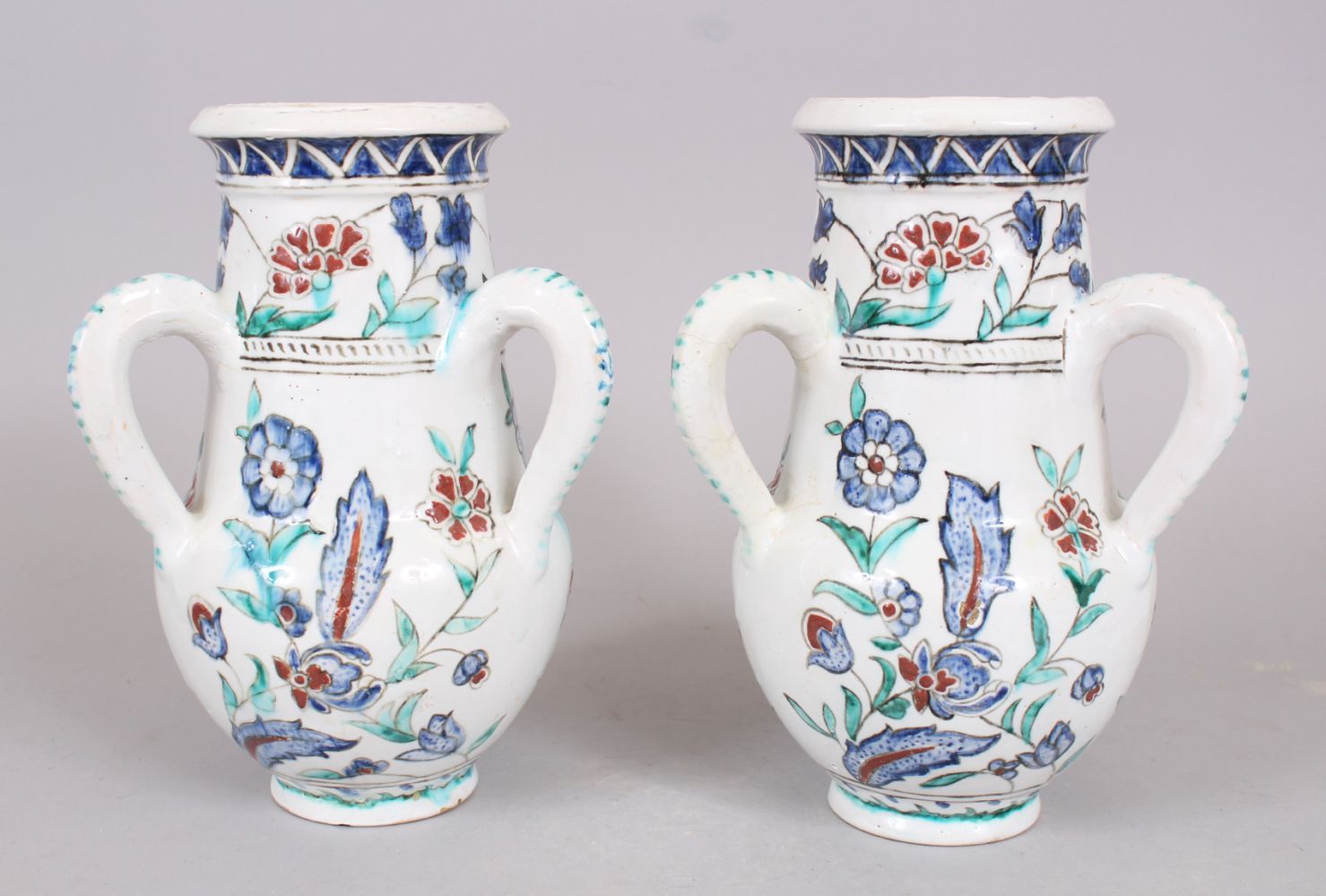 A PAIR OF IZNIK STYLE POTTERY THREE HANDLED VASES, 25cm high.