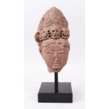 A 12TH CENTURY CARVED STONE HEAD wearing a band of skulls, mounted on a stand.10ins long.