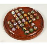 A WOODEN SOLITAIRE BOARD, with a complete set of "air twist" marbles. 20cms diameter.