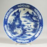 A CIRCULAR PLATE, decorated in blue and white with figures on a bridge. 23cms diameter.