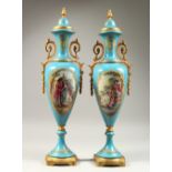 A PAIR OF SEVRES STYLE PALE BLUE GROUND SLENDER VASES AND COVERS, painted with reverse panels of