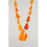 AN AMBER NECKLACE, comprising one large central naturalistic form bead and thirty graduated