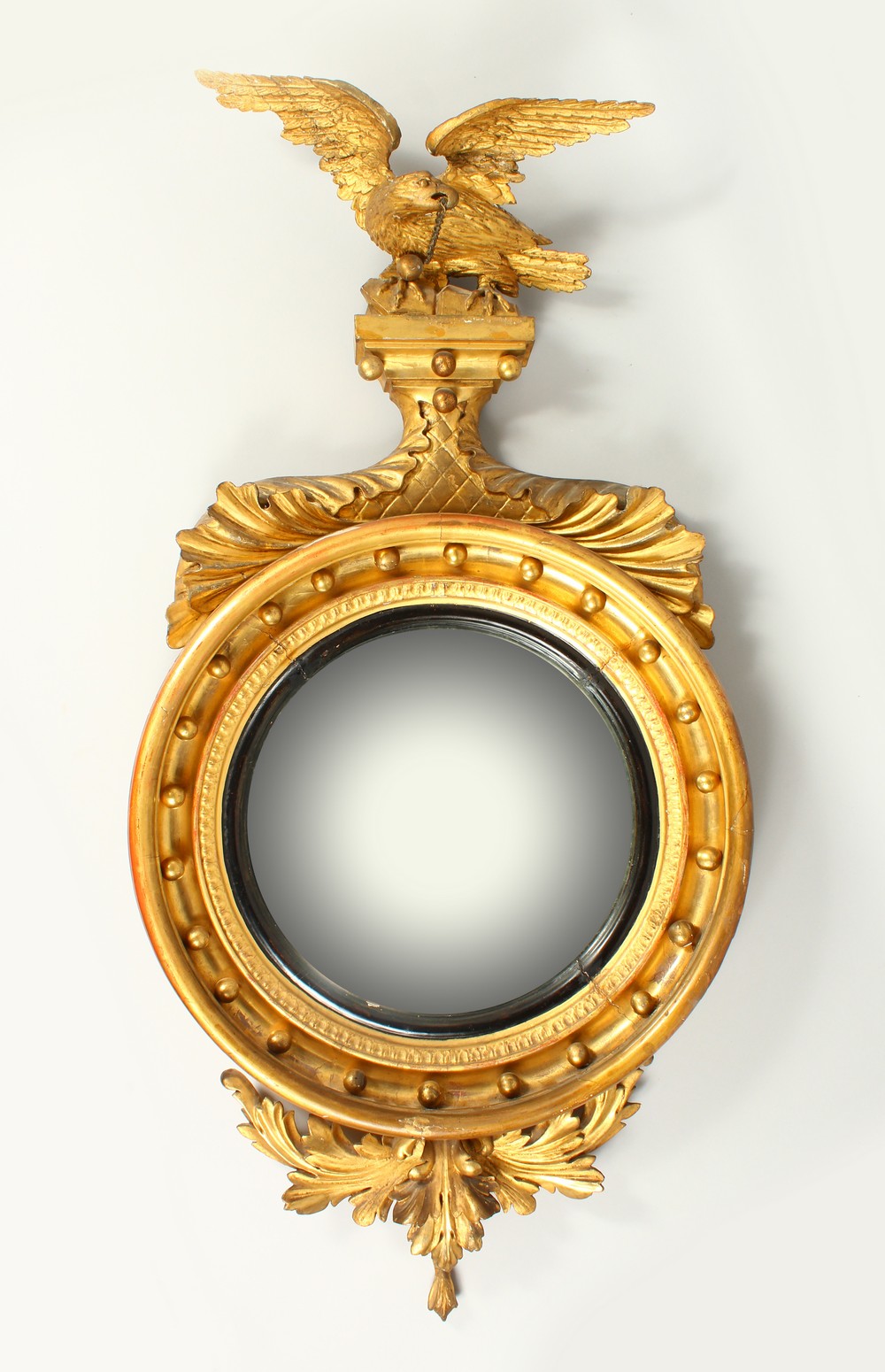 A REGENCY GILTWOOD CONVEX WALL MIRROR, with eagle cresting, ball applied frame, and leaf carved