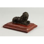A SMALL CAST BRONZE MODEL OF A RECUMBENT LION, on a red marble plinth. 14cms long.