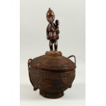 A TRIBAL WOVEN BASKET AND COVER, with carved wood figural handle. 42cms high.