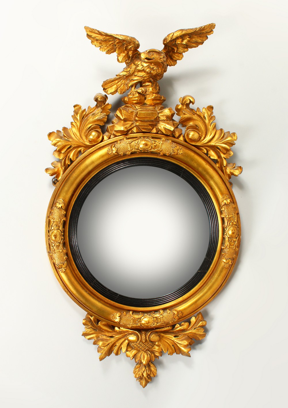 A REGENCY GILTWOOD CONVEX WALL MIRROR, with eagle cresting and leaf carved frame. 102cms high x