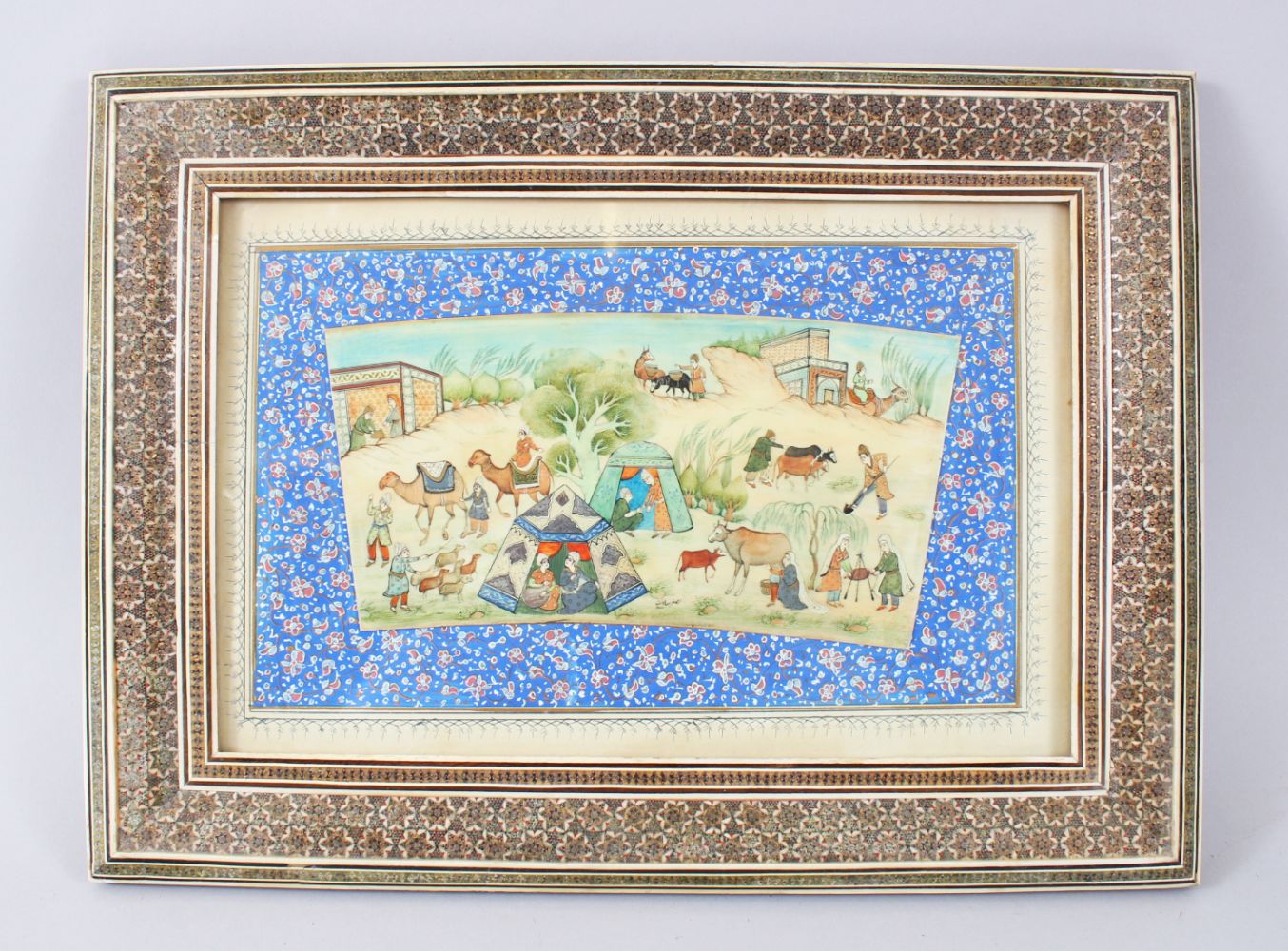 A PERSIAN PAINTING ON IVORY, tents, figures on camels and cows, 10cm x 20cm in a mosaic frame.