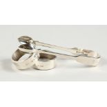 A PAIR OF PLAIN SILVER SERVIETTE RINGS and A PAIR OF SUGAR TONGS.