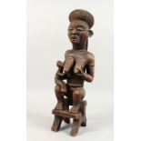 A LARGE CARVED WOOD TRIBAL FIGURE, mother and child seated on a stool. 21.5ins high.