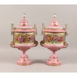 A PAIR OF SEVRES STYLE PINK GROUND TWIN-HANDLED PEDESTAL URNS AND COVERS, with floral decoration.