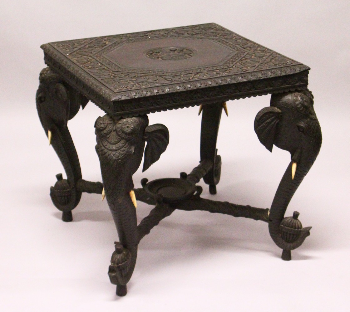 AN EARLY 20TH CENTURY CEYLONESE CARVED EBONY LOW TABLE, with an elephant head leg to each corner.