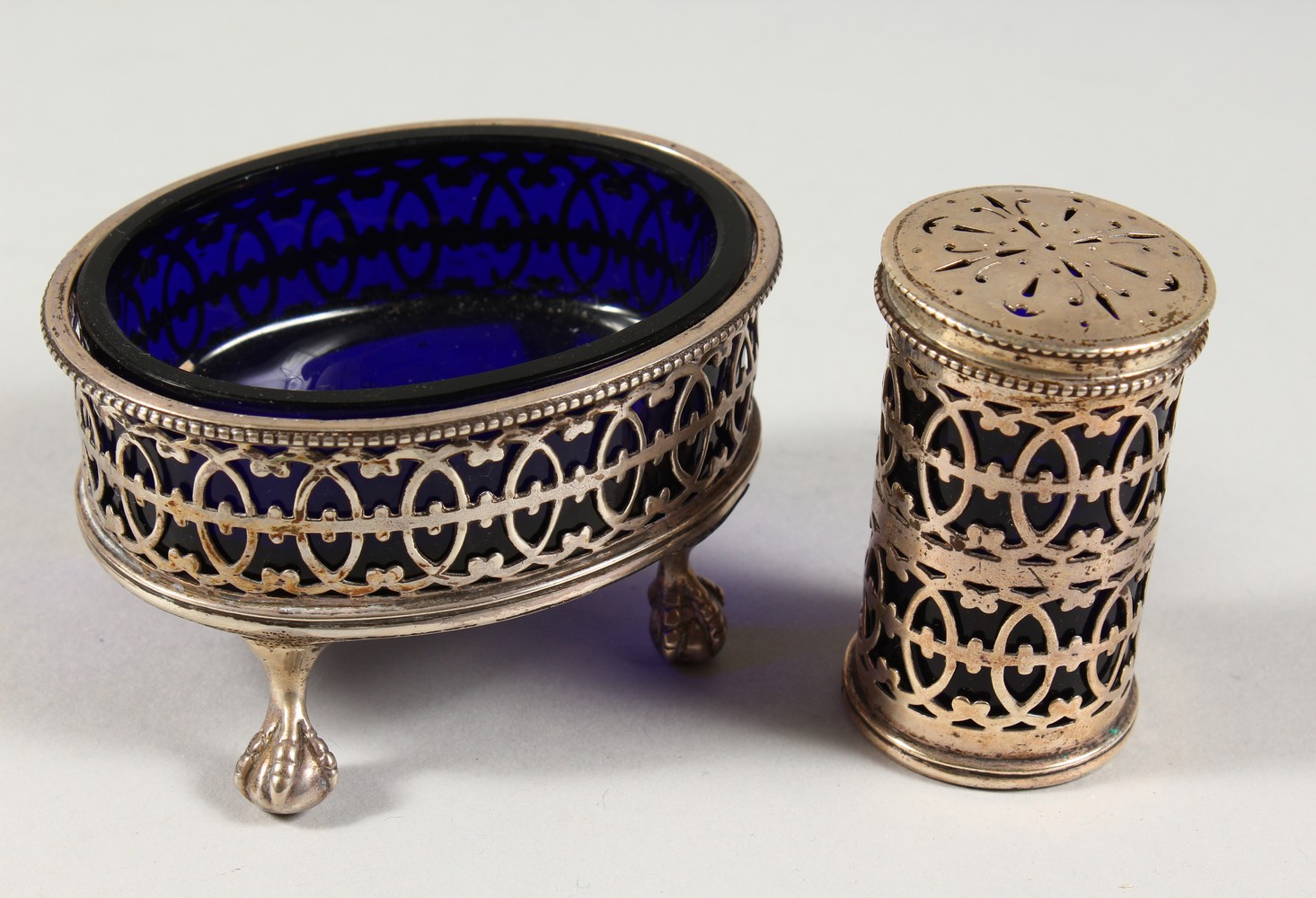 AN OVAL PIERCED SALT CELLAR with sapphire blue liner, London 1942, and A PEPPERETTE, London 1907 (