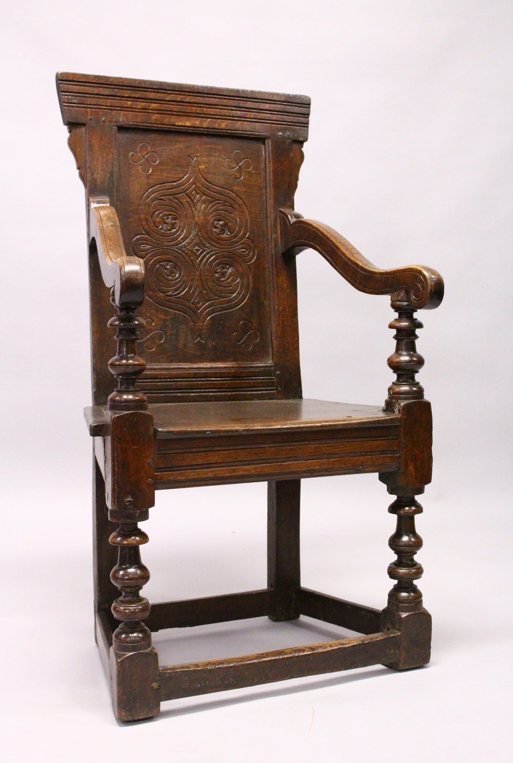 AN 18TH CENTURY OAK WAINSCOT ARMCHAIR, with carved back, solid seat and curving arms and turned