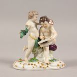 A SMALL MEISSEN GROUP OF TWO CUPIDS, "Scribe", on a flower encrusted base. Cross swords mark in