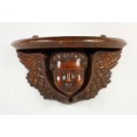 A WOODEN WALL BRACKET, carved as a winged cherub head. 13.5ins wide.