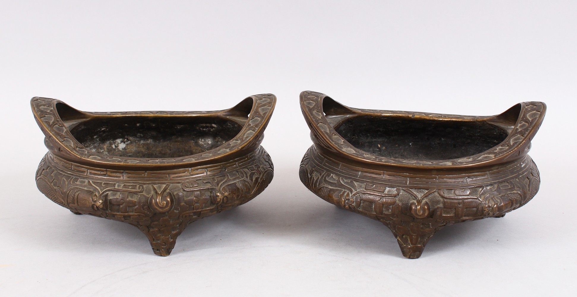 TWO GOOD CHINESE BRONZE TRIPOD CENSERS, Both with deep carved scenes of chilongs and archaic design,