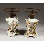A PAIR OF CONTINENTAL PORCELAIN LAMP BASE, with cupids and encrusted with flowers. 9ins high.