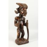 A CARVED WOOD TRIBAL STANDING FIGURE, of a man with headdress, holding a staff. 23ins high.